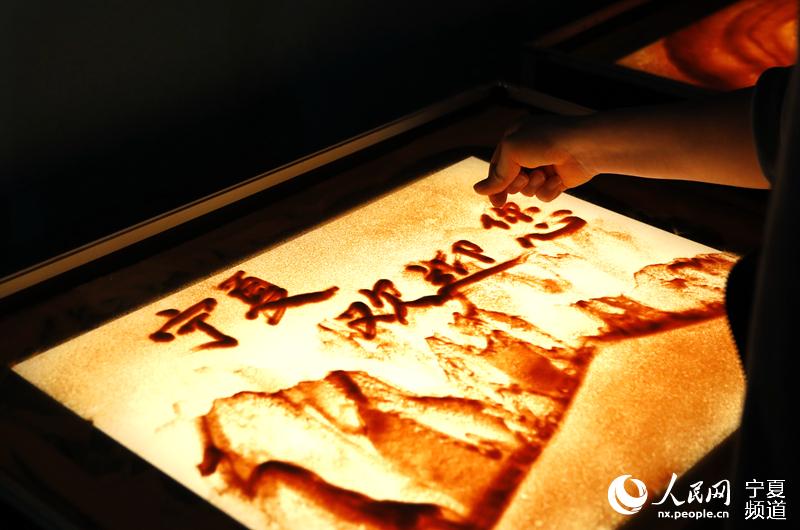 沙画师正在沙画上写上“宁夏欢迎您”字样。人民网 高嘉蔚摄
