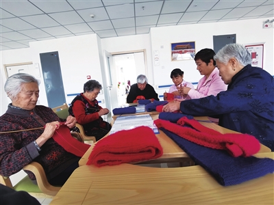 老人们围坐桌前，边织围巾边哼着歌。本报记者  马荣   摄