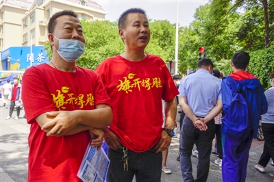     两位爸爸穿着写有“旗开得胜”的T恤，到考点迎接孩子。