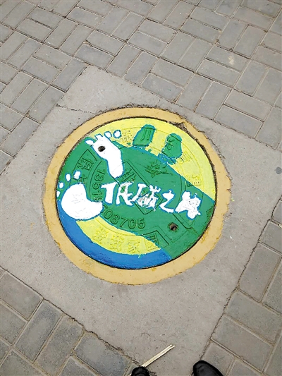 手在井盖上涂鸦,画出一幅幅美丽的图画,向人们传播绿色环保等文明理念