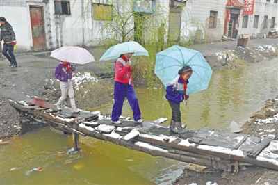 <p>学生们下雨天走过临时搭建在红花渠上的木“桥”。（摄于2015年）</p>