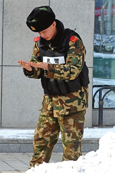 2月13日,解放军某部一名执勤武警战士换岗后用雪搓揉冻僵的手指.