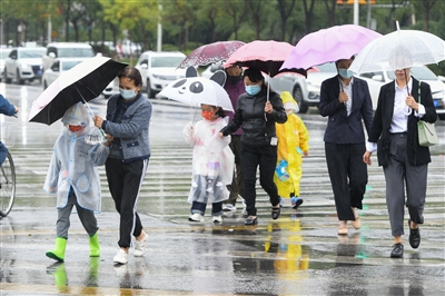 9月19日，在银川市金凤区正源北街，家长们冒雨送孩子上学，一名家长努力把伞偏向孩子，自己却被雨水淋湿。             本报记者  季正  摄