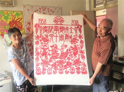 两位老人展示剪纸作品。